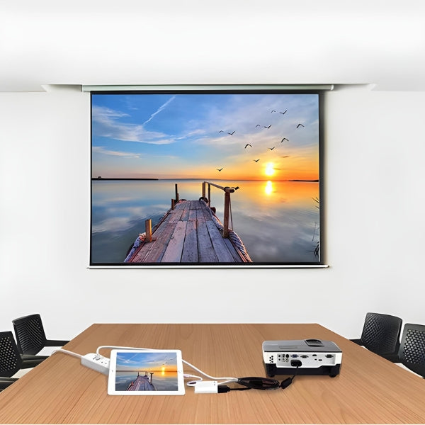 A conference room with a wooden table, chairs, and a tablet using The Projection Room’s Lightning To HDMI Cable to mirror content in 1080p HD—displaying a dock at sunset with flying birds on the projector.