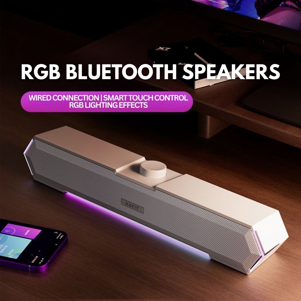 The Projection Room RGB Bluetooth Speakers sit on a desk near a smartphone and monitor, featuring smart touch control, dazzling RGB lighting effects, and wired 3.5MM audio jack connectivity.