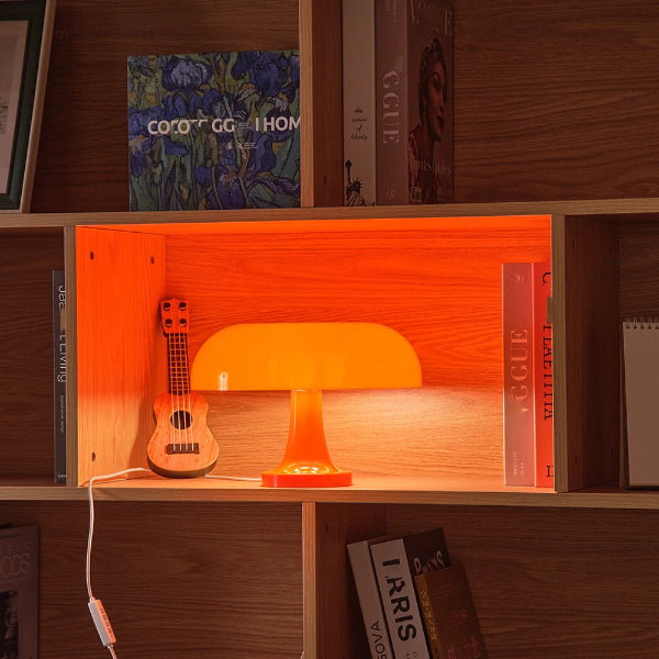 A small wooden shelf displays The Projection Room’s Modern Danish Mushroom Table Lamp (LED Bedside Lamp) and a miniature guitar amid upright books. The dimmable LED casts a warm glow, illuminating the cozy wood-paneled shelves.