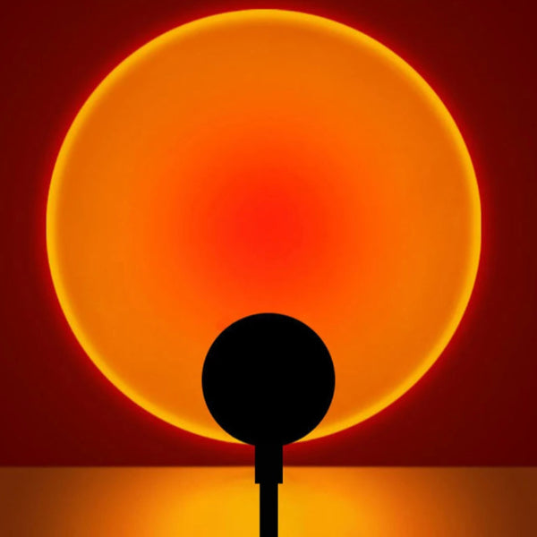 The black silhouette stands before the Sunset Glow LED Lamp by The Projection Room, its vibrant orange-red circle resembling a glowing sun against a dark backdrop with modern lighting effects.