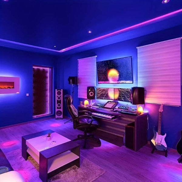 A modern music studio featuring The Projection Room’s USB LED Light Strips RGB (15m, Smart Control) in purple and blue, studio monitors, a keyboard on the desk, a large screen with digital art, an electric guitar, and a cozy sofa with a coffee table.