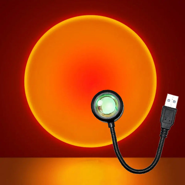 The Projection Rooms Sunset Glow LED Lamp is a portable USB device with a flexible neck, creating modern lighting effects by projecting gradient patterns of sunset hues from bright yellow to deep orange and crimson red on reflective surfaces.