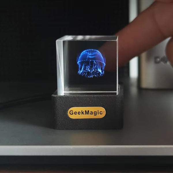 The Projection Rooms 3D Icon Desk Light Decor displays a glowing blue jellyfish in a clear cube on a dark base. Mobile app control allows for customizable content, providing an interactive experience with a fingertip touch.
