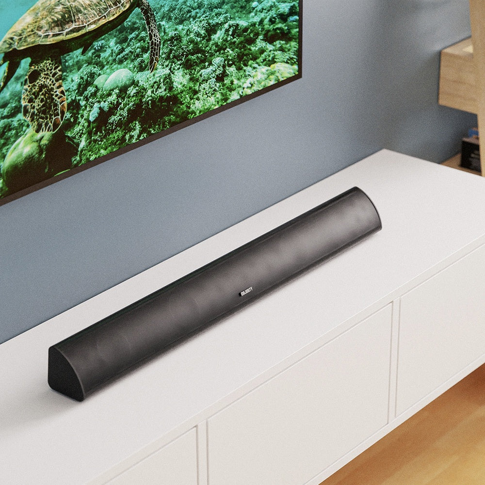 A sleek black Majority Snowdon II Soundbar by The Projection Room with Bluetooth sits on a white entertainment unit, in front of a wall-mounted TV showing a sea turtle swimming underwater, complemented by a wooden shelf to the right.