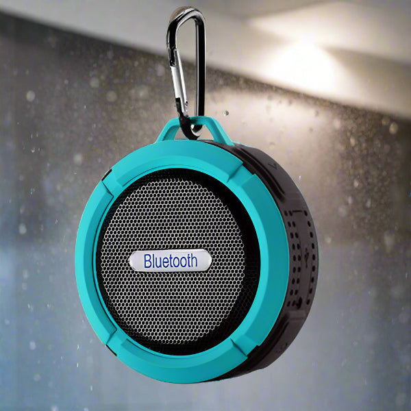 A blue and black Portable Waterproof Wireless Mini Bluetooth Music Speaker by The Projection Room hangs by a carabiner, showcasing its splash-proof design. Its circular shape with a mesh front promises an impressive high-fidelity sound experience against a blurred droplet background.