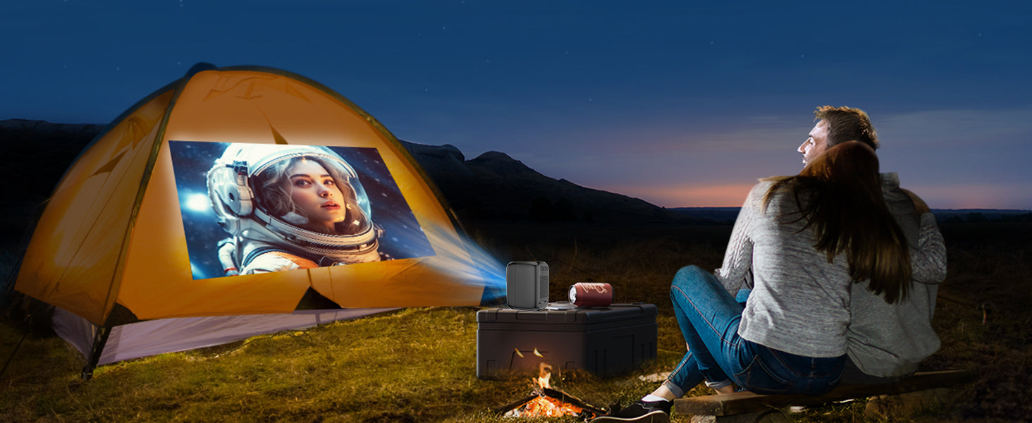 A couple enjoys a starry movie night with The Projection Rooms PocketCinema HD projecting space explorer scenes on their tent, perfectly casting the film against majestic mountains from a small table beside them.